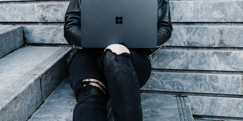 woman in black jacket and black pants sitting on concrete stairs usingMicrosoft Surface Laptop  